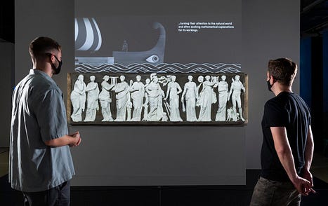 Visitors in Ancient Greeks Science and Wisdom watch a projection on ancient sarcophagus panels showing the Muses, Apollo & Athena © Science Museum Group
